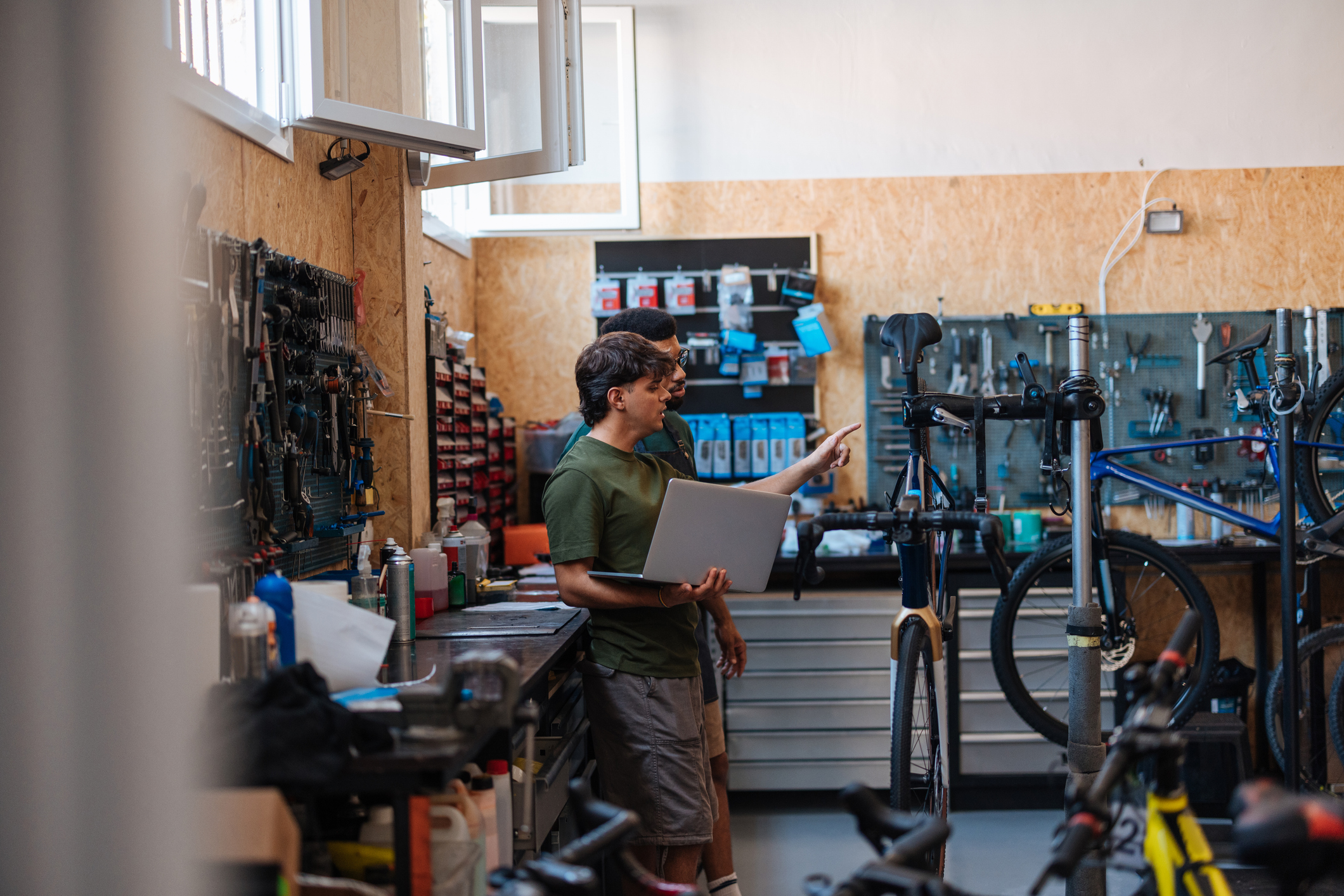 A mechanic in a workshop holding a laptop as they survey the bikes to work on