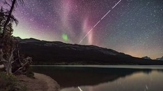 a streak of light stretches across a starry night sky above a lake
