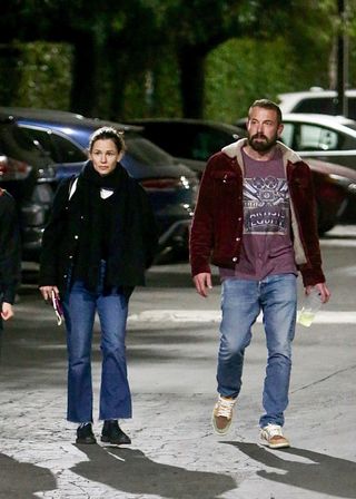 Jennifer Garner wearing jeans and a black coat walking in a parking lot at night next to Ben Affleck wearing jeans and a red jacket