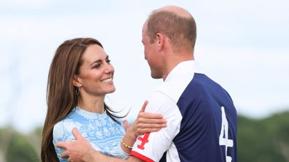 Kate Middleton wearing a blue dress and hugging Prince William who is wearing a a white and blue polo jersey