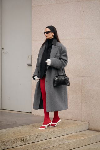Guest wearing a gray coat with a black dress and red tights in Milan.