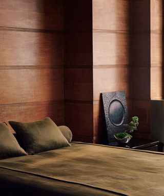 bedroom with wood paneling and rich olive bedding, side table, black mirror