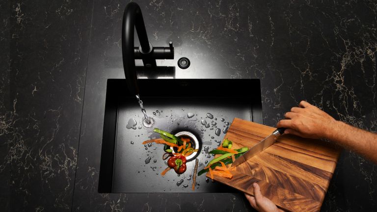 A man with chopping board and knife with food waste over a sink with an InSinkErator Evolution 250 food waste disposer