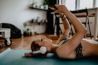 A womay lays on a yoga mat while looking at her smart phone