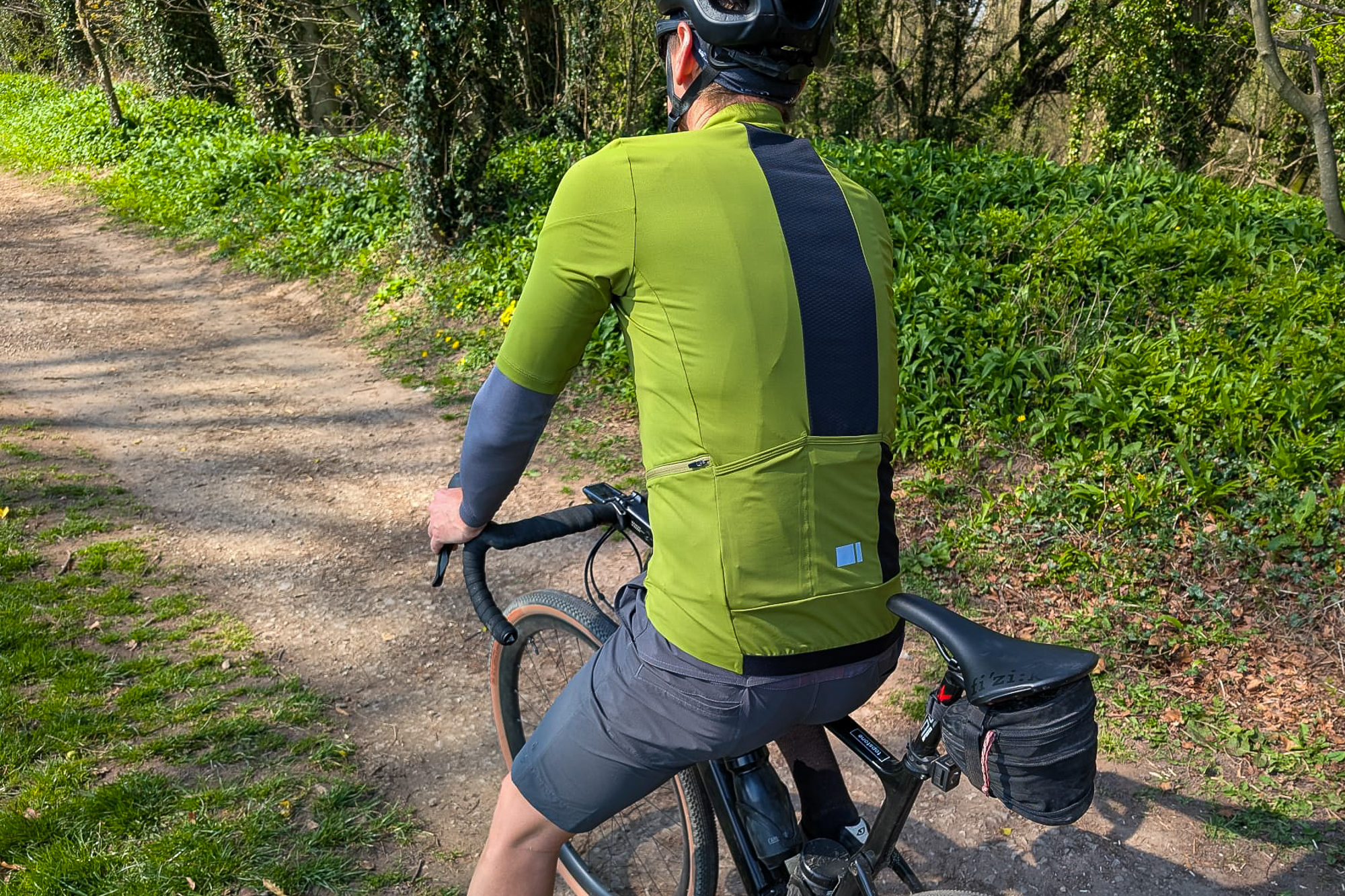 Rear shot of a stationary rider wearing a green jersey and black helmet on a canal towpath