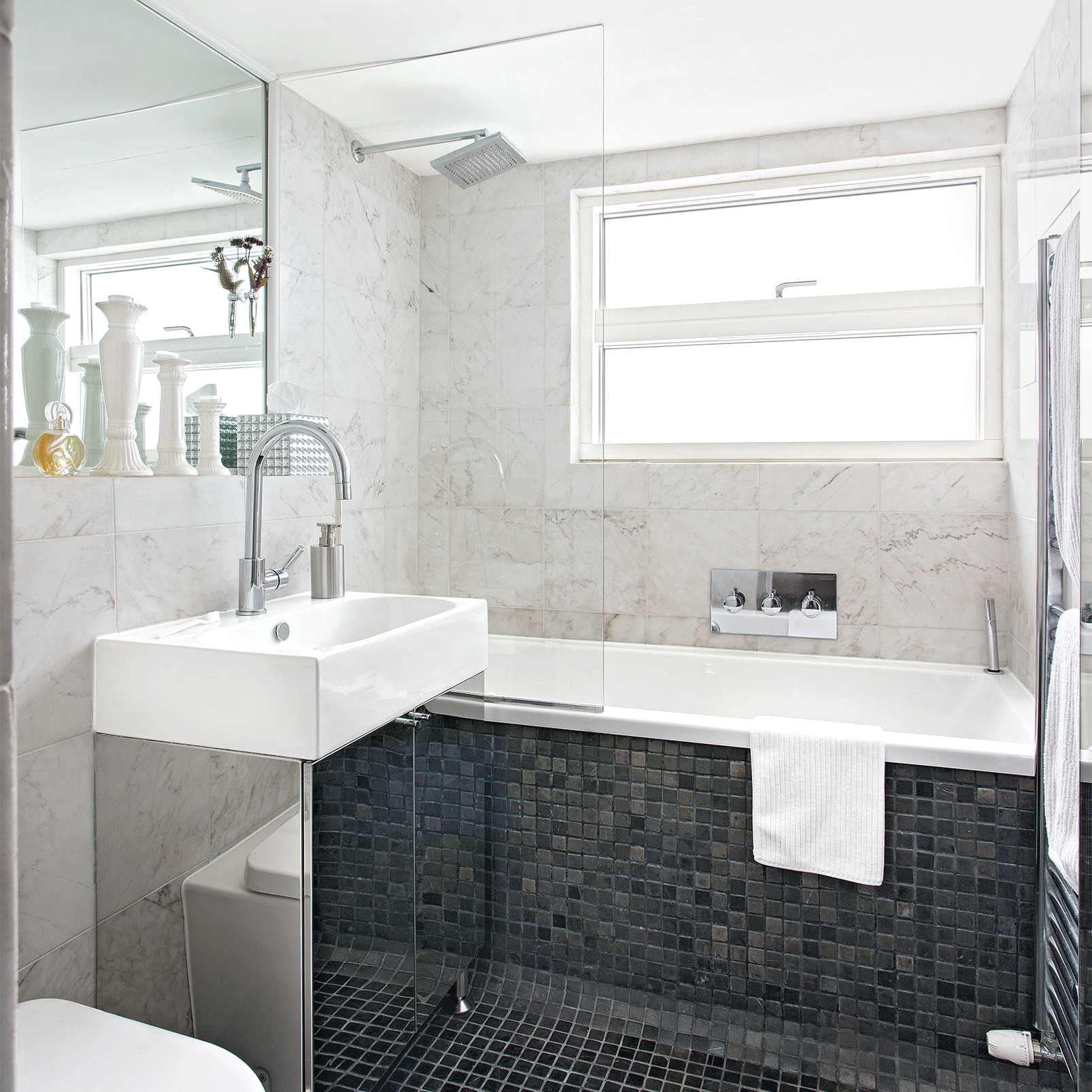 bathroom with marble wall tiles and sleek black mosaic tiles on the floor and side of the bath
