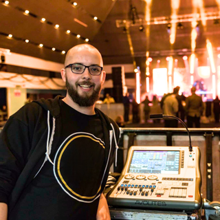 Smiling headshot of Luke Edwards in front of a mixing console with a stage as the backdrop.