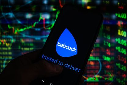 Babcock logo seen displayed on a smartphone with stock market percentages in the background