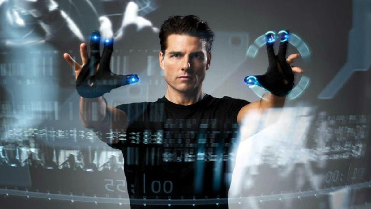 A man is wearing special gloves that allow him to control the futuristic computer using his hands. Floating in front of him are images and words.
