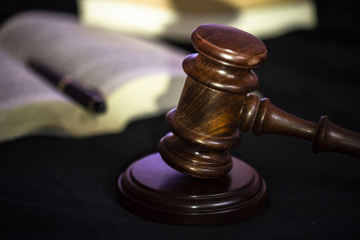 A wooden gavel in the foreground with an open book an a pen in the background