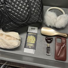 airport bin with handbag, headphones, passport, and more in it. 