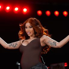 a woman performing onstage wearing long, red hair and a brown sleeveless bodysuit