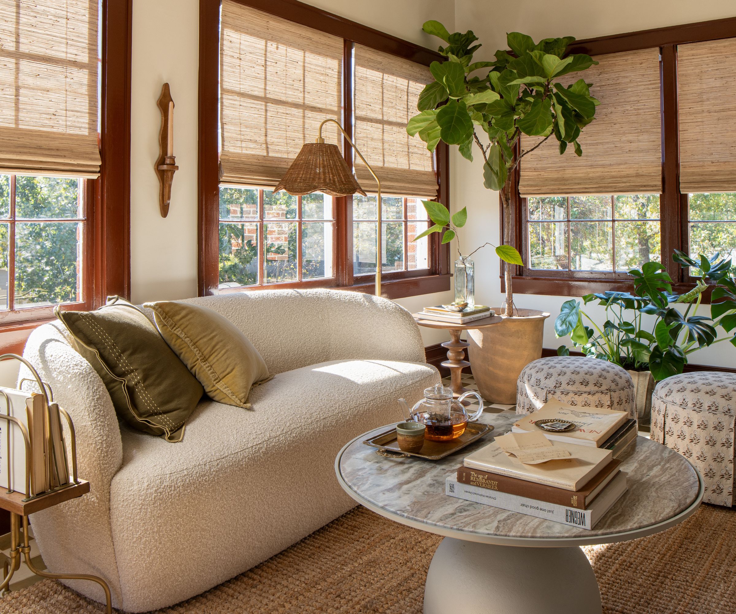 Sunroom with rattan blinds, jute rug, curved boucle sofa, marble coffee table and large potted plant