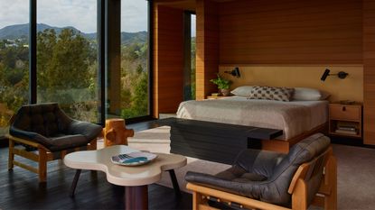 mid century modern bedroom with timber panelling, built-in bed with yellow headboard and wall sconces, and a seating area with mid-century modern style leather chairs around a coffee table