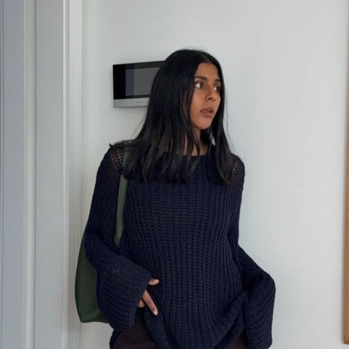 Monikh wears a navy sweater and a green shoulder bag.
