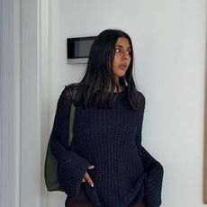 Monikh wears a navy sweater and a green shoulder bag.