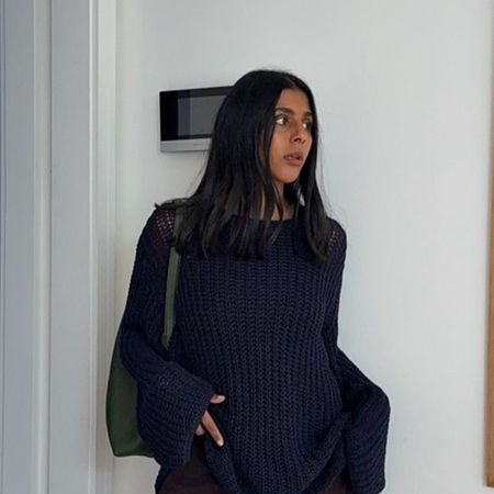 Monikh wears a navy sweater and a green shoulder bag.