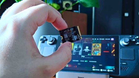 Hand holding WD Black SN770M SSD with Steam Deck in backdrop