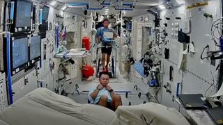 two astronauts exercise inside a white-walled space station.