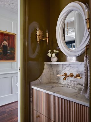 green bathroom with marble and timber fluted vanity, and round white mirror