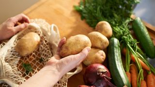 Woman's hands holding a selection of potatoes over chopping board with other vegetables