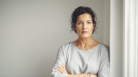 A thoughtful, attractive older woman crosses her arms and looks into the camera. 