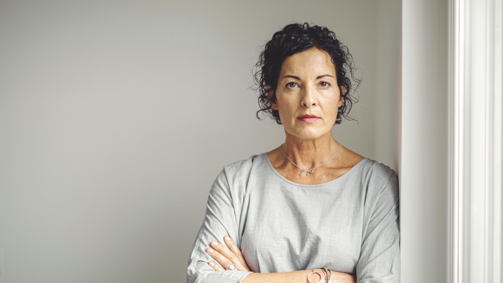 A thoughtful, attractive older woman crosses her arms and looks into the camera. 