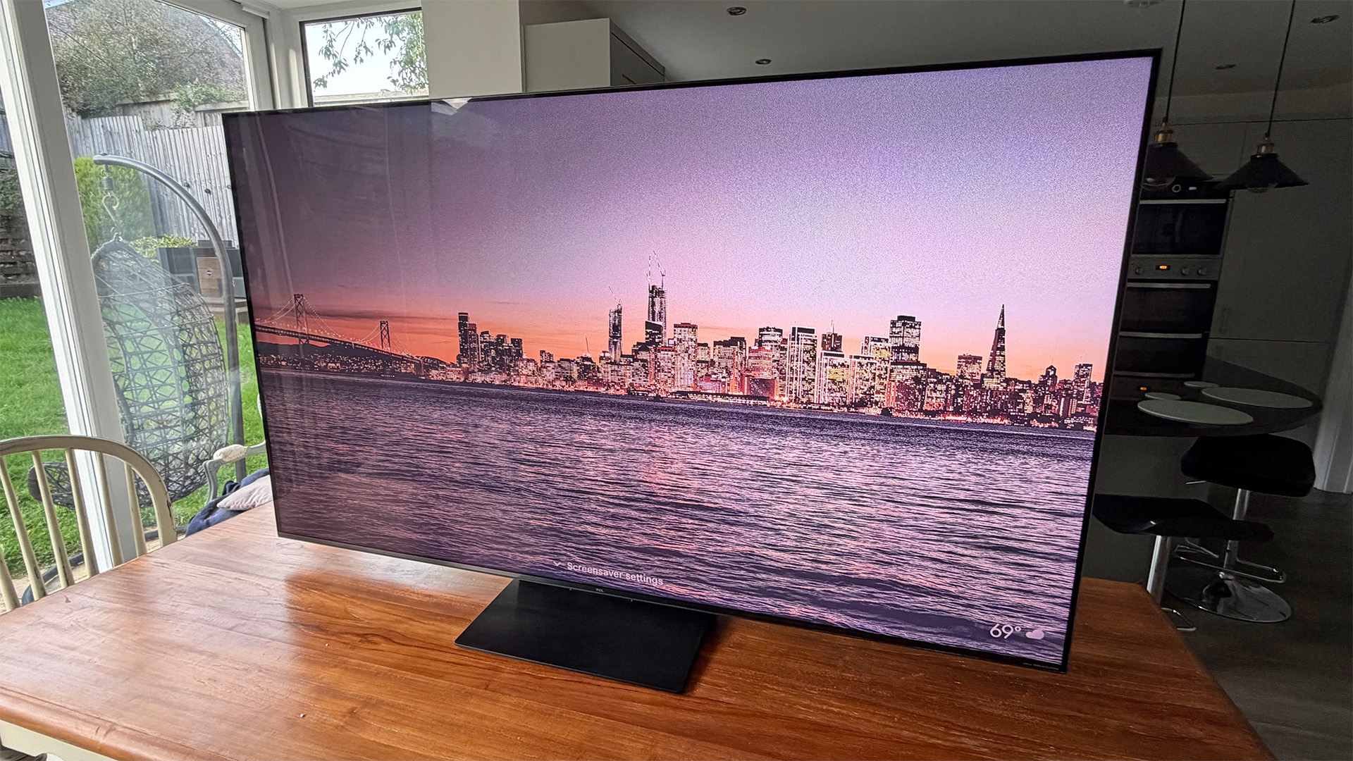 TCL C7L Mini LED TV on wooden dining table on screen is city skyline