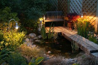 decking with small bench and pond at night with garden sleepers