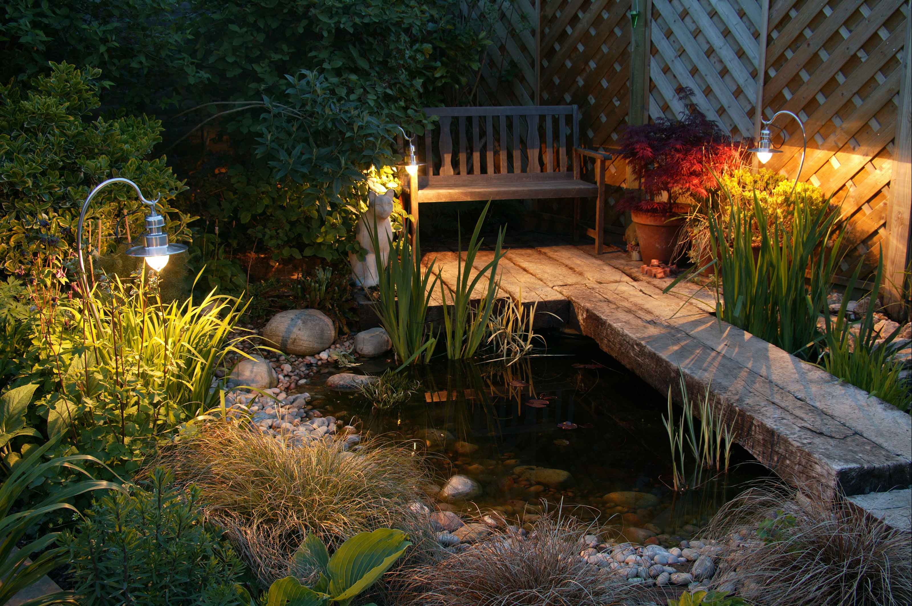 decking with small bench and pond at night with garden sleepers