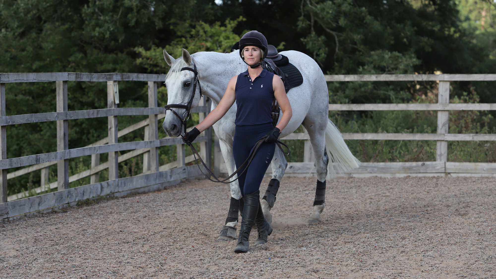 Rider walking grey horse in hand in arena
