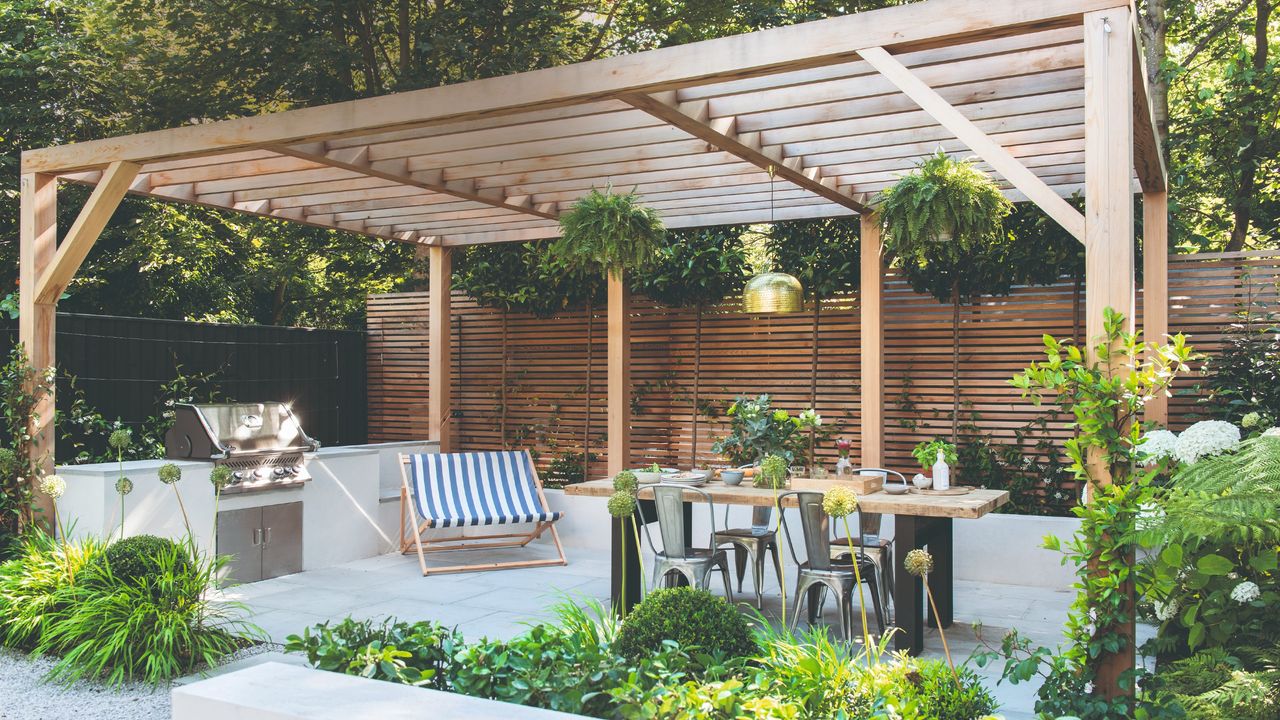 Covered outdoor kitchen area with wooden pergola, BBQ and dining area with table and chairs