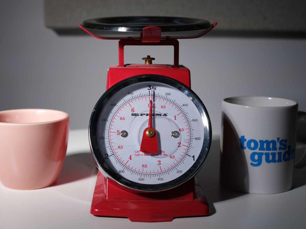 An image of a red scale and two coffee cups, one with the Tom's Guide logo