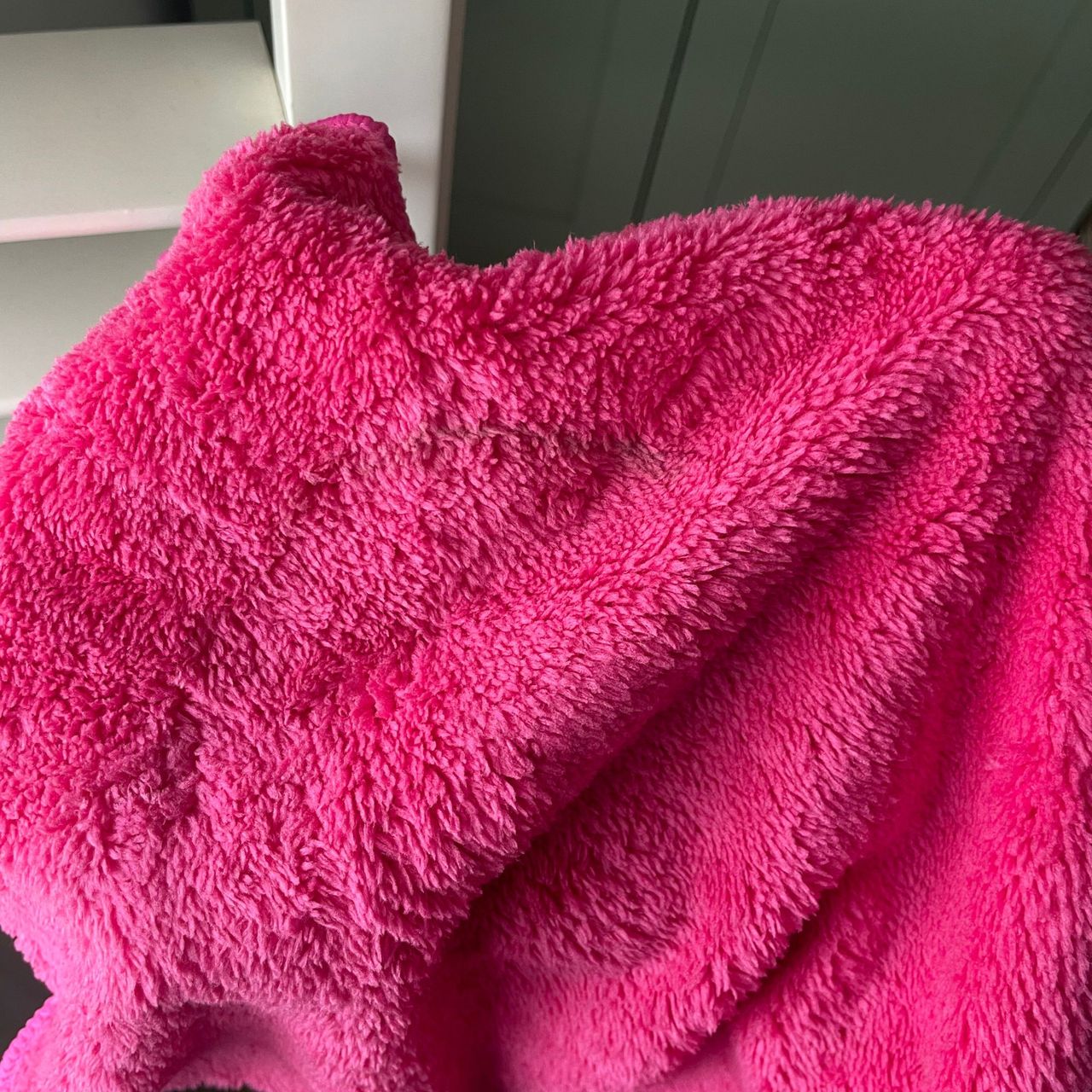 Hand holding pink Minky duster to the camera, with plantation shutters in the background