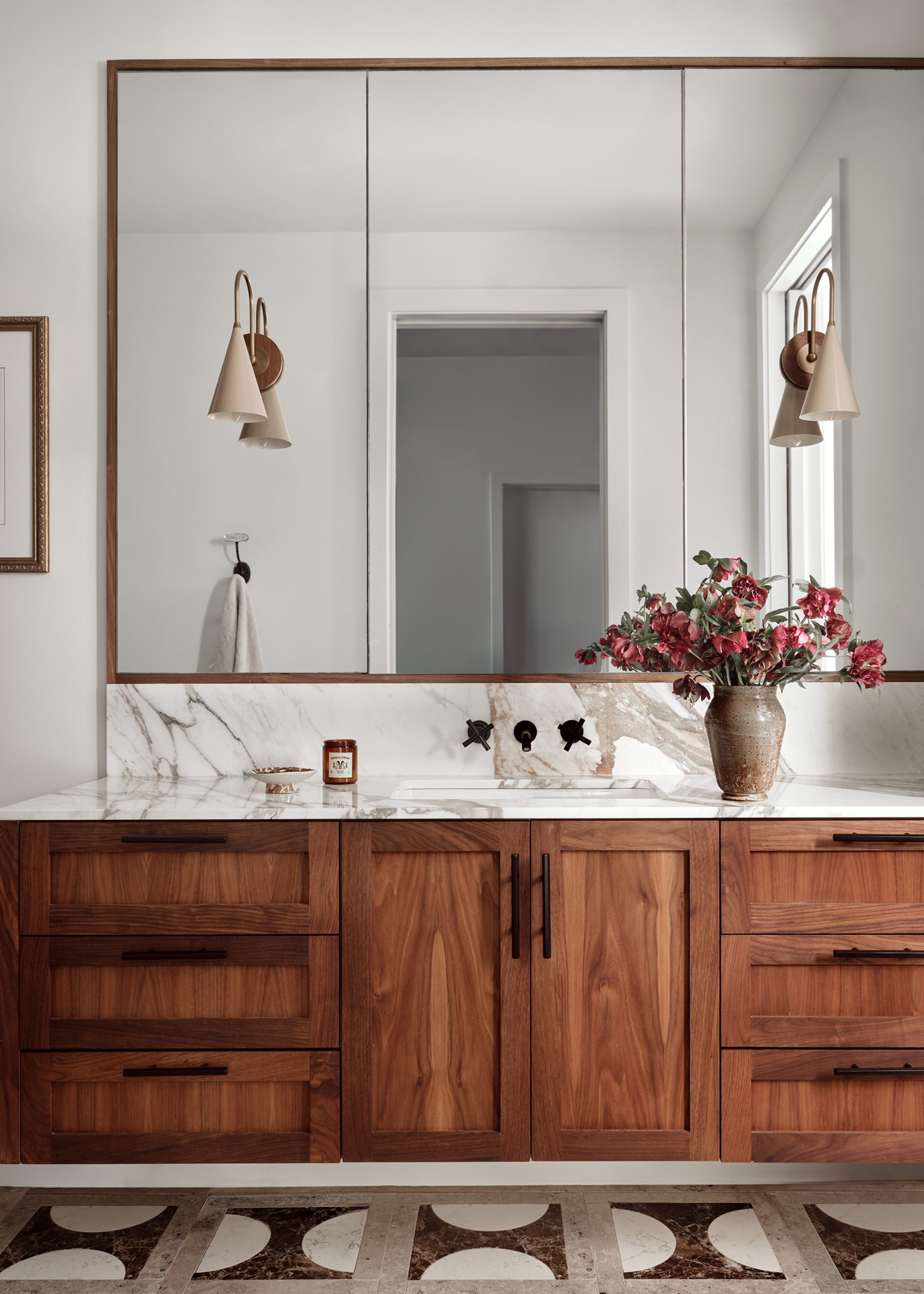 A bathroom with drawers and marble tile floors and a big mirror with two scones on it