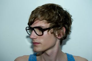 Male model in blue vest and dark framed glasses looking down to the left