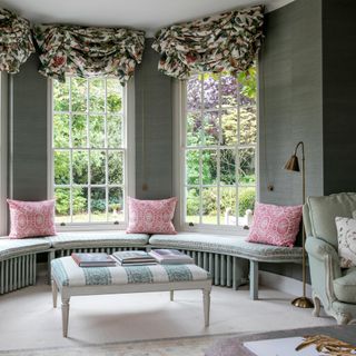 grey living room with large bay window and window seat with pink cushions
