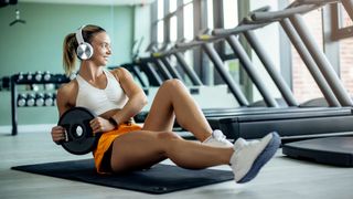 Woman performs core exercise in gym holding a small weight plate