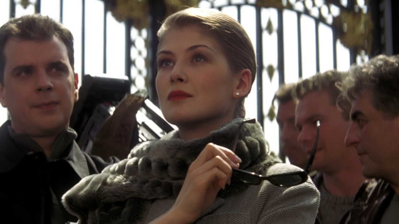 Rosamund Pike stands looking up while holding her sunglasses in Die Another Day.