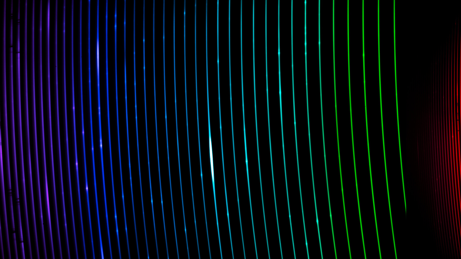 A series of brightly coloring curved colored lines creating strips of rainbow over a dark black background