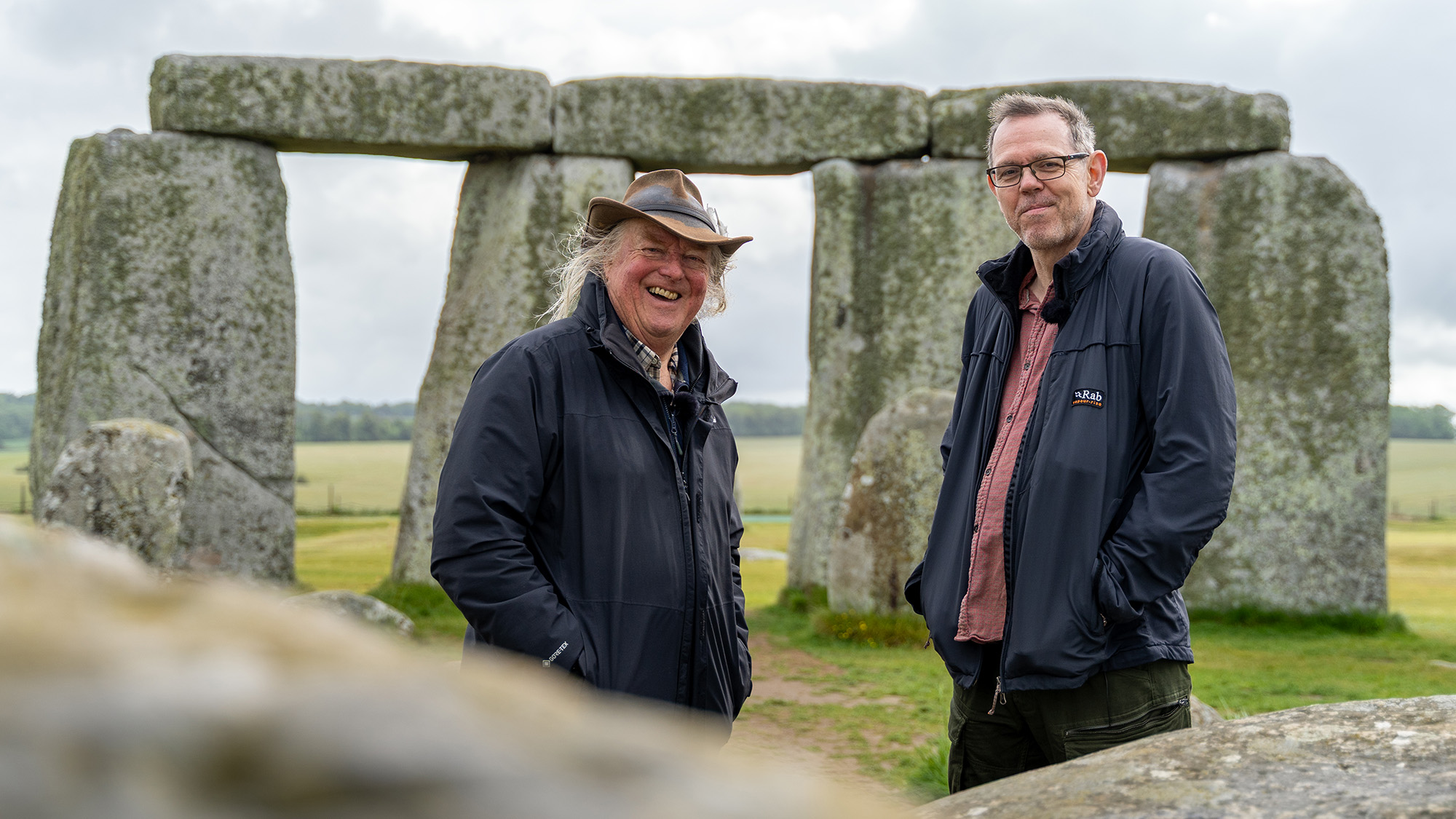 To older men stand next to the vertical stones of Stonehenge