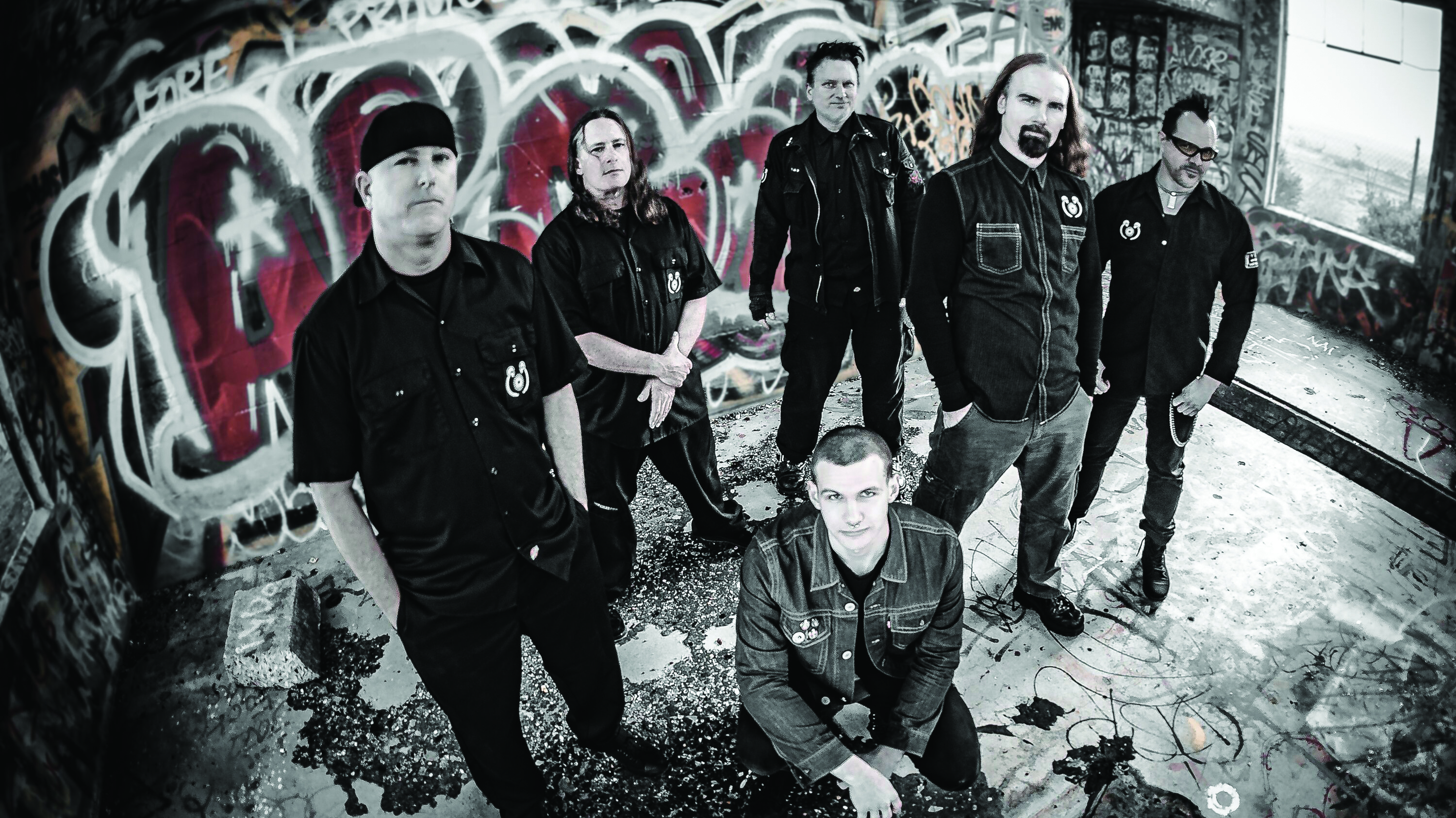 A press shot of Mudface taken in 2016, stood in front of a graffiti wall