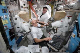 Expedition 61 commander Luca Parmitano and flight engineer Drew Morgan work inside the Quest airlock aboard the International Space Station while dressed as Apollo flight controllers as a tribute to the 50th anniversary of the Apollo 12 moon landing mission on Thursday, Nov. 14, 2019.