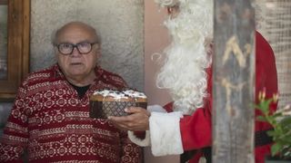 A still from A Sudden Case of Christmas showing Danny DeVito as Lawrence, stood next to someone dressed as santa