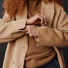 A person in a beige coat and a brown top from GAP.