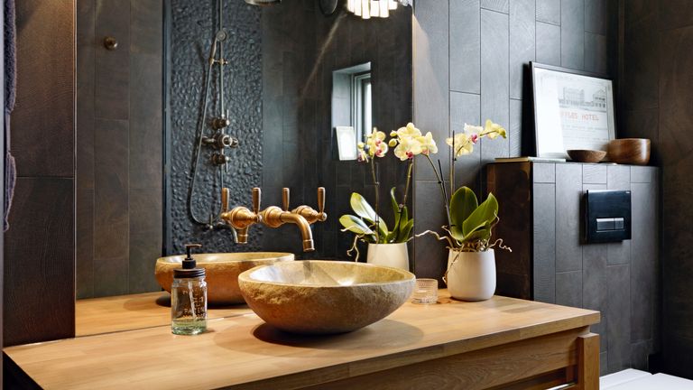black spa style bathroom with mirrored wall and wooden vanity with stone basin