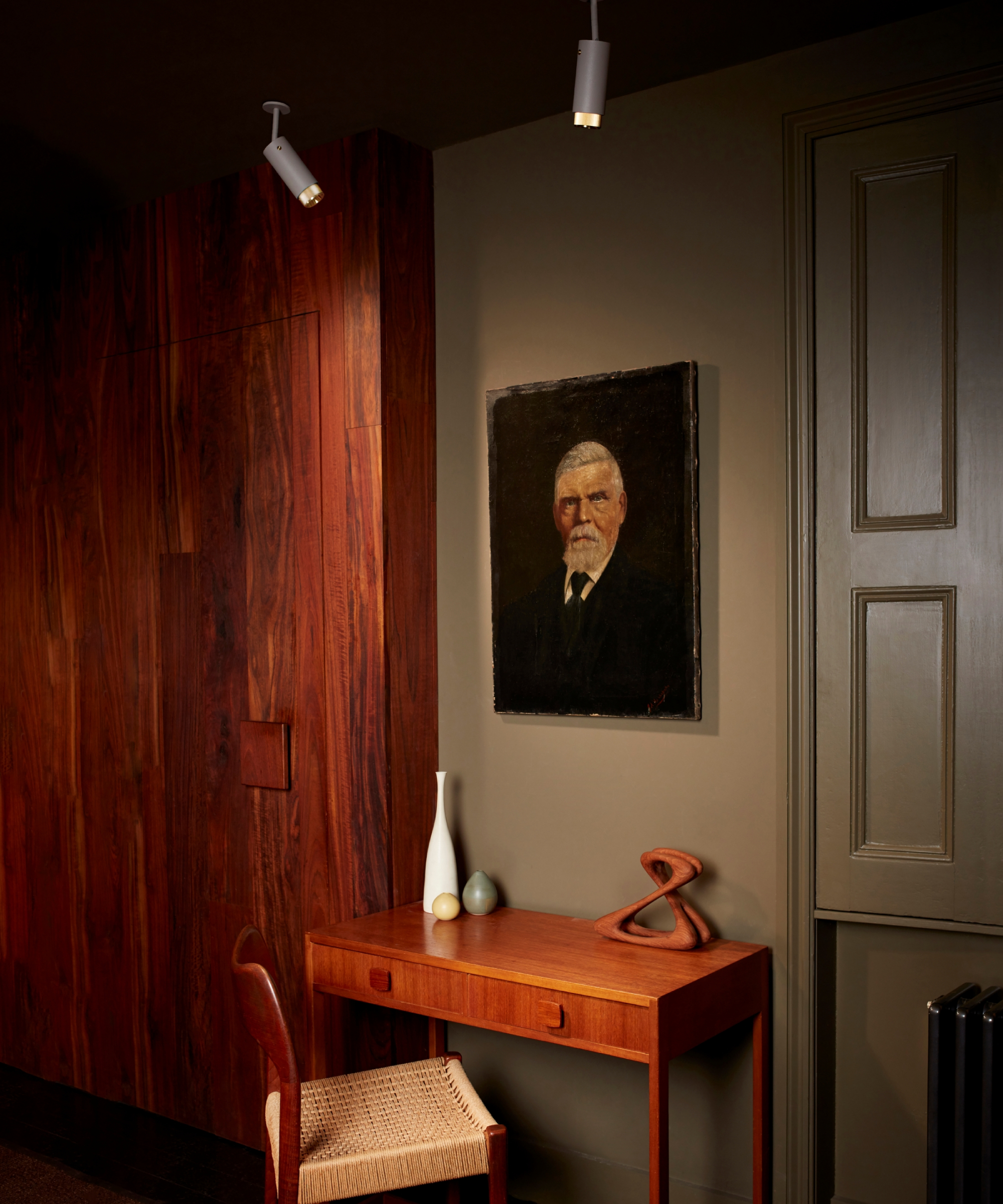 desk in room with wooden cupboards, green walls, portrait on wall and directional spotlights in ceiling
