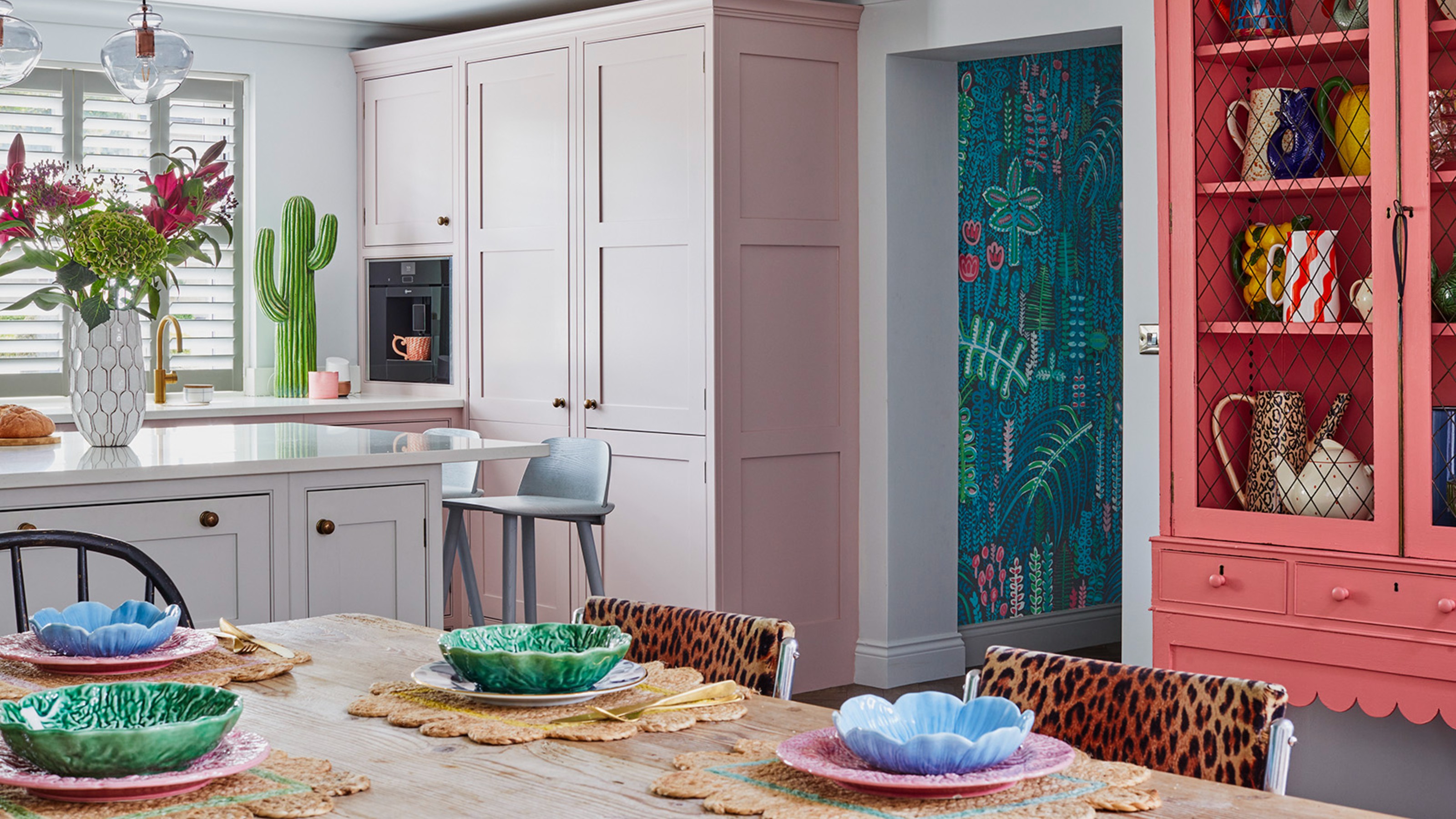 A pink kitchen with a decorative cactus and an open-plan dining area with leopard-print chairs and cabbage bowls on the table