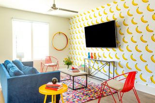 Teenage playroom ideas with colorful and fun banana print wallpaper, blue and red seating and multicolored rug.