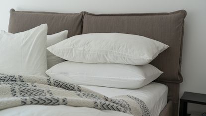 White pillows stacked in a bed with a taupe headboard and geometric knitted throw on top